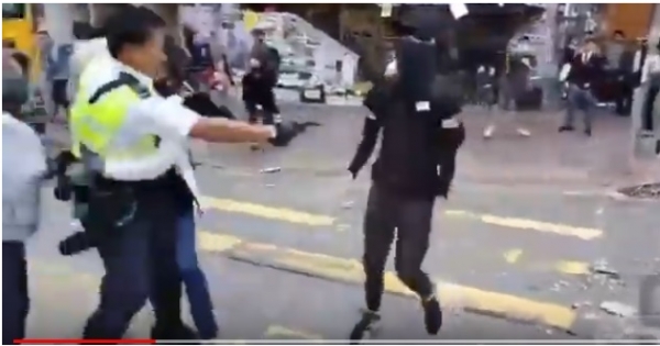 홍콩 사이완호 지역에서 11일 오전 경찰 한 명이 검은색 옷을 입고 얼굴을 가린채 다가오는 시위 참가자를 향해 총을 쏘고 있다. 이 사람은 실탄에 맞아 부상을 입은 것으로 전해지고 있다. 사진은 유튜브 동영상을 캡처한 것이다.