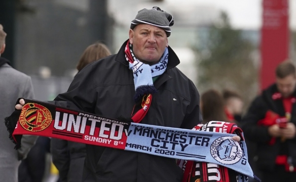 A merchandise seller holds out a scarf for fans to buy ahead of the English Premier League soccer match between Manchester United and Manchester City at Old Trafford in Manchester, England, Sunday, March 8, 2020. (AP Photo/Dave Thompson)